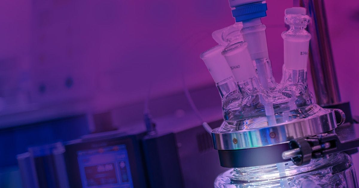 Laboratory setup with flasks and scientific equipment illuminated in purple light, highlighting advanced research technology.