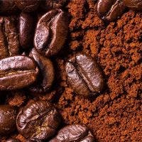 Close-up image of roasted coffee beans interspersed with ground coffee. The beans have a shiny appearance, indicating a fresh roast.