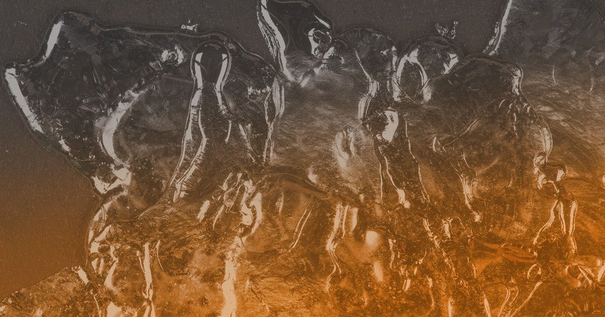 A close-up image of a translucent, textured surface with a mix of grey and orange hues, resembling an abstract artwork or frozen ice.