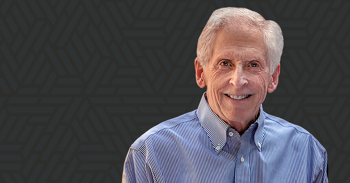 Elderly man with short white hair and a smile, wearing a blue and white striped button-down shirt, against a dark geometric background.