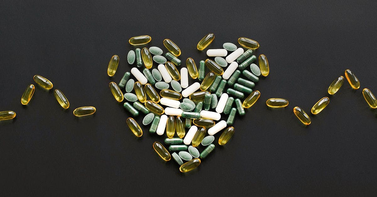 Various capsules and tablets arranged in the shape of a heart on a black background, with additional capsules forming lines on either side.