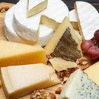 A variety of cheese including brie, hard cheese, and blue cheese, arranged on a wooden board with walnuts and grapes.