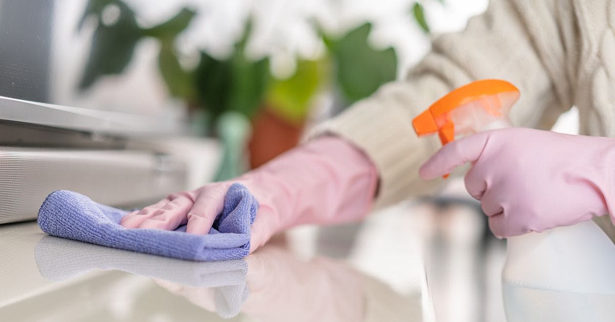 Person in pink gloves cleaning a kitchen counter with a spray bottle and blue cloth.
