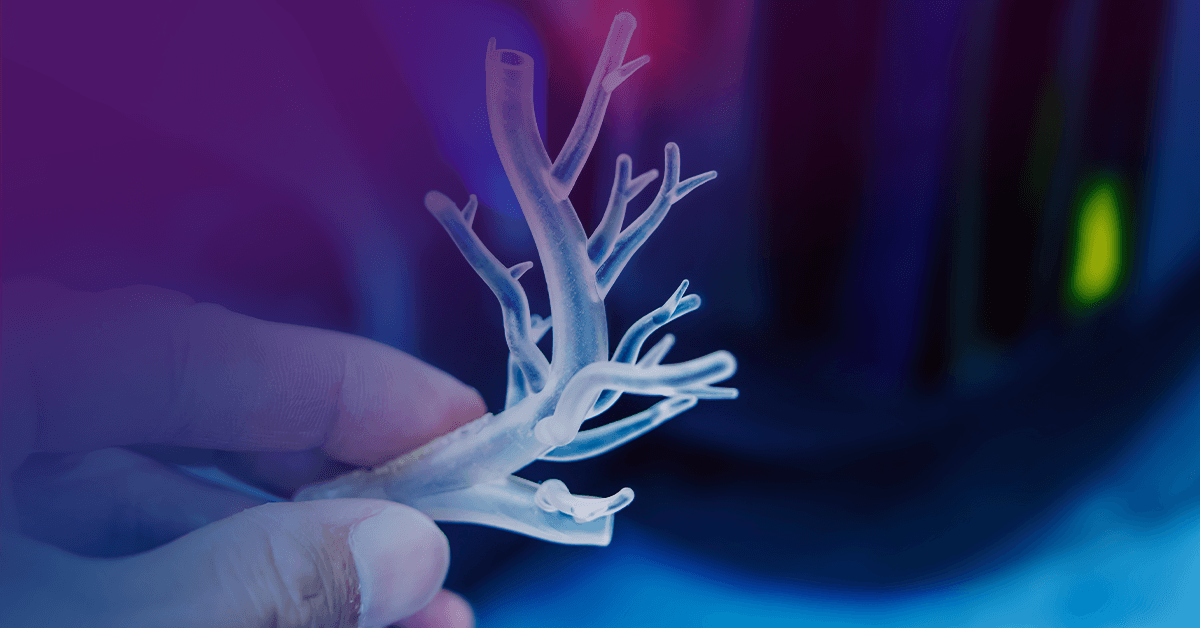 A person holds a translucent, branching 3D-printed object resembling a small tree or coral against a blurred background with a blue and purple glow.