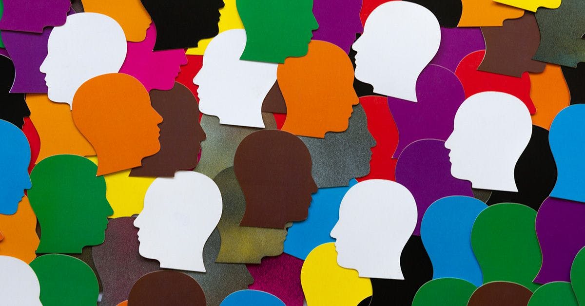 A collage of variously colored silhouette cutouts of human heads, arranged in a scattered manner against a flat surface.
