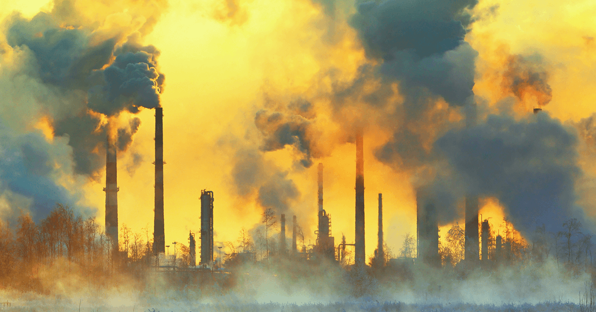 Industrial plant emitting large amounts of smoke and air pollution with a yellowish sky in the background.