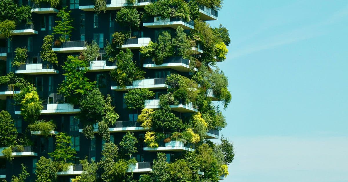 A modern building facade with numerous trees and plants on its balconies against a clear blue sky.