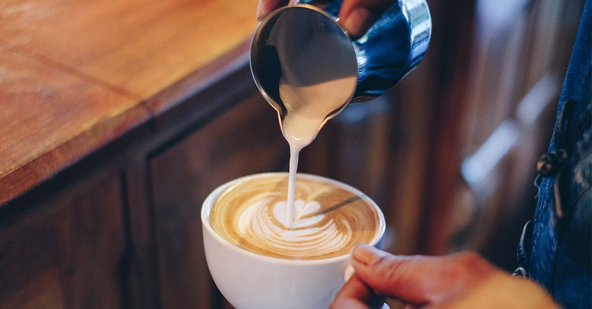 A barista pours steamed milk into a cup of coffee, creating latte art.