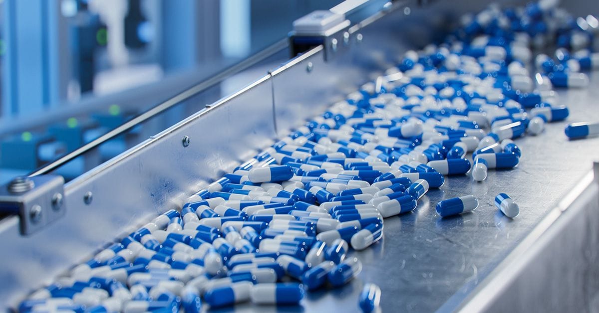 A conveyor belt in a factory transports numerous blue and white capsules.