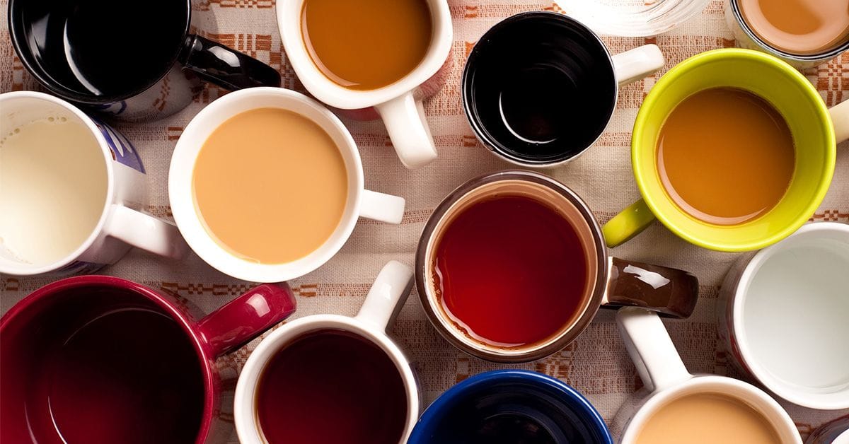 An aerial view of various mugs of different sizes and colors on a wooden table, each with a different type of beverage such as coffee, tea, juice, milk, and water.