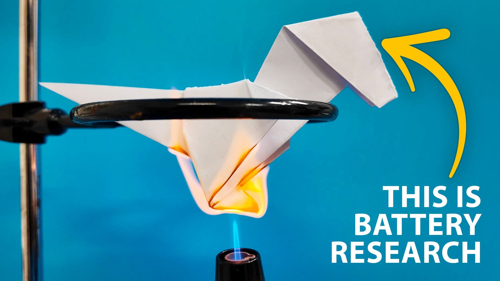 An origami paper t-rex held over a flame in a lab setup, with text reading ‘This is battery research'