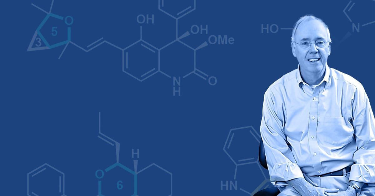 A man sitting in front of a blue background with a molecule in front of him.