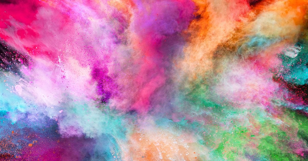 A vibrant explosion of colorful powder, blending shades of pink, orange, blue, and purple against a dark background.