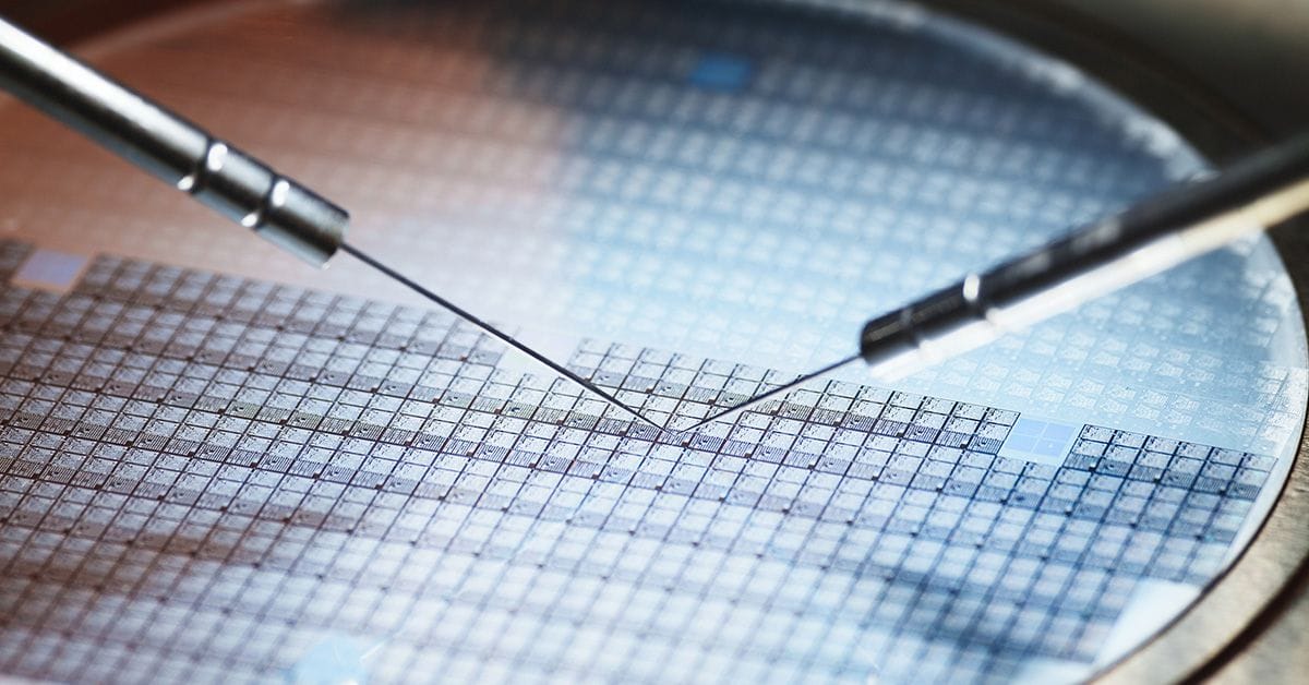 Two precision needles poised above a silicon wafer, showcasing a grid of intricate microchip patterns.
