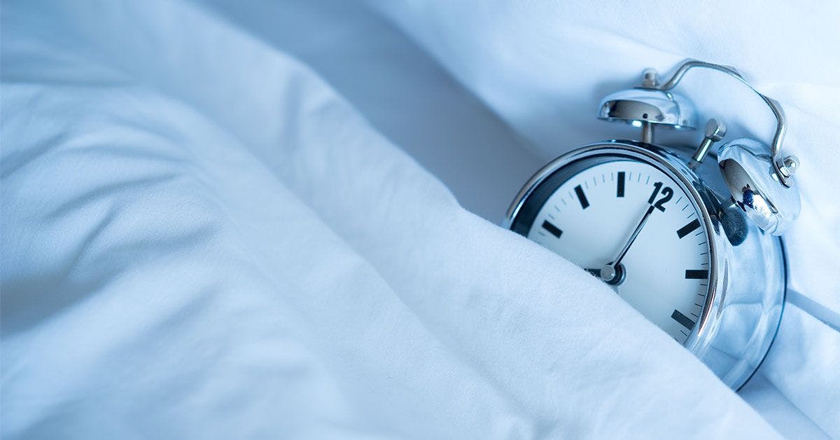 A silver alarm clock peeking out of a white sheet.