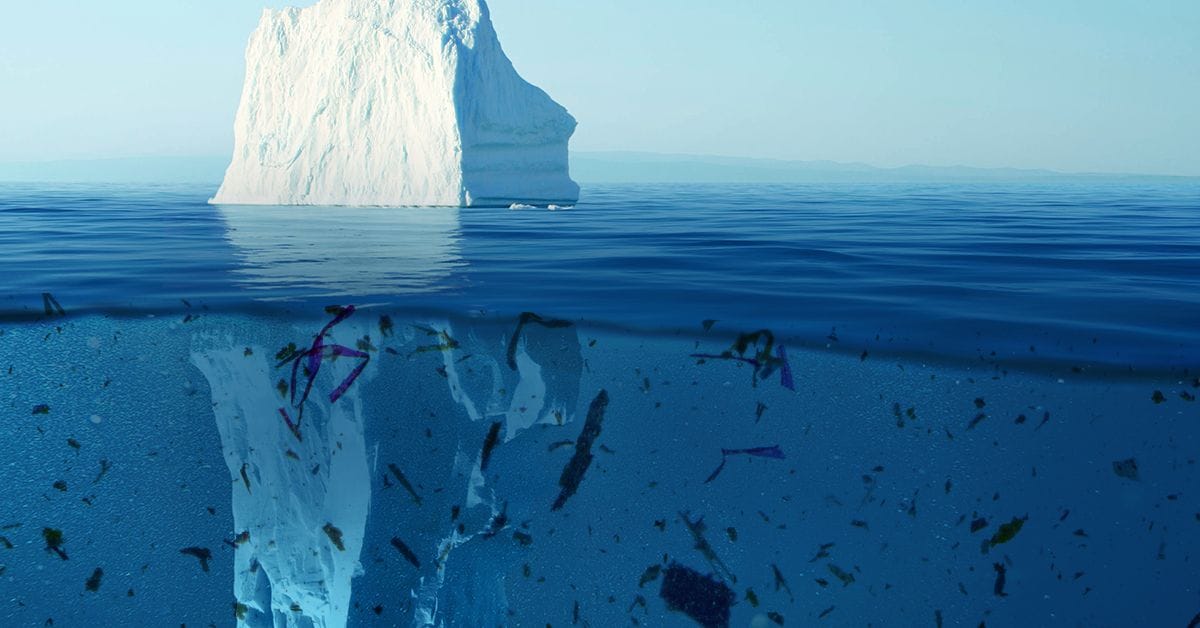 An expansive iceberg in the ocean, encircled by floating microplastics, illustrating the impact of pollution on marine environments.