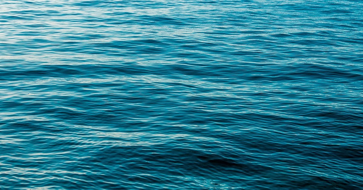 The surface of a calm ocean, with small flowing waves in various shades of blue.