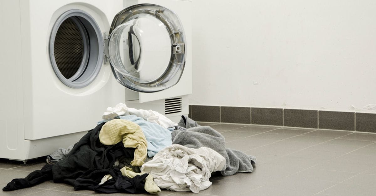 A pile of dirty laundry next to an open front-loading washing machine with a circular door.