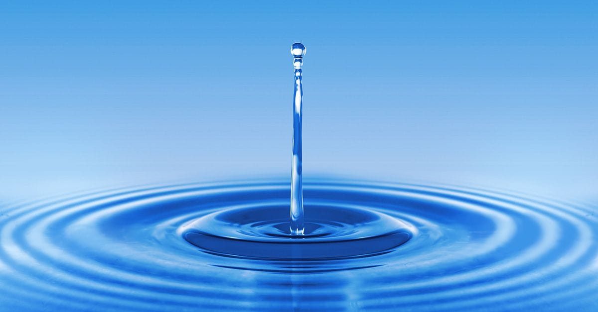 A water droplet rising above a smooth, rippling surface with a serene blue background, capturing the essence of tranquility.