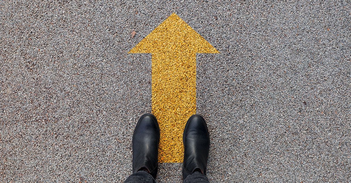 A person's feet standing on a yellow arrow.