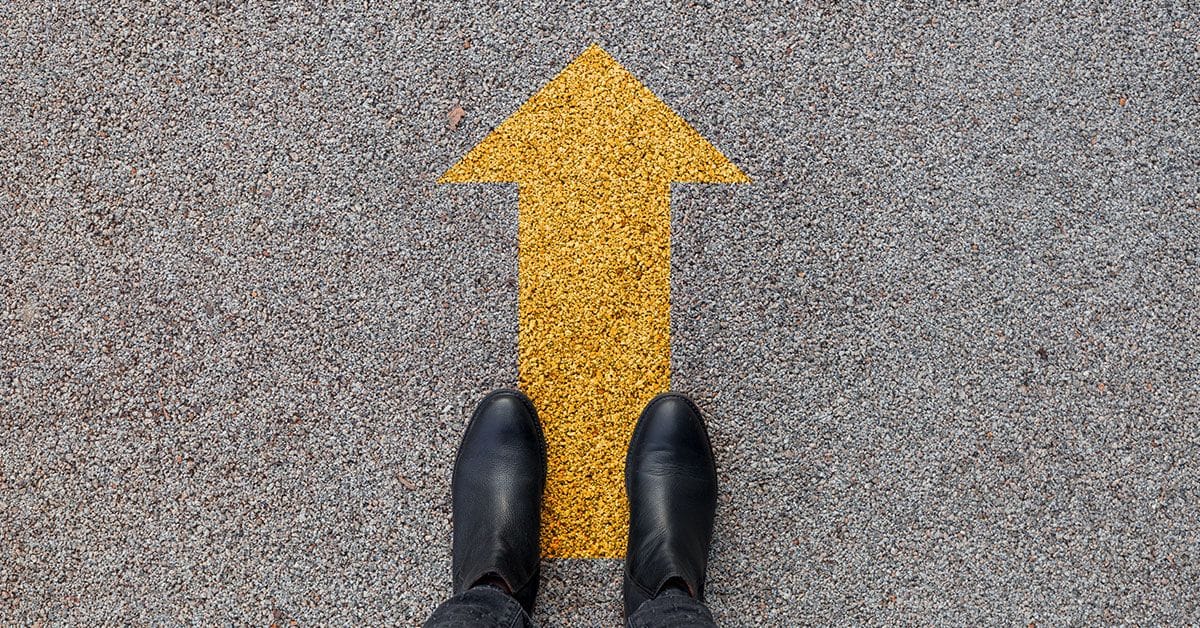 A person's feet standing on a yellow arrow.