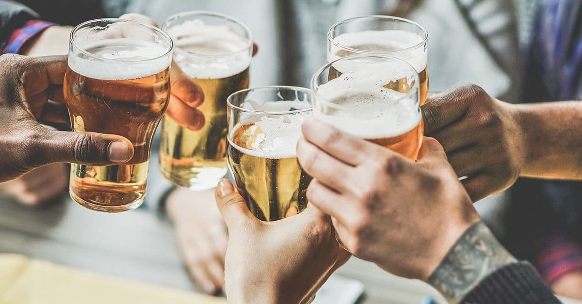 Five people clinking glasses of beer over a wooden table.