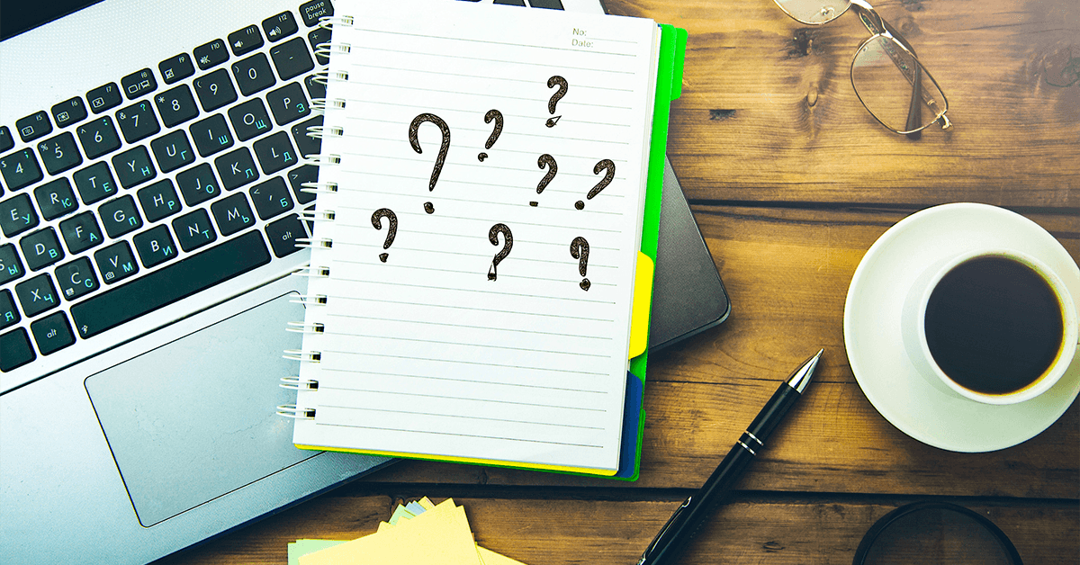 question marks on notepad with keyboard and coffee on table