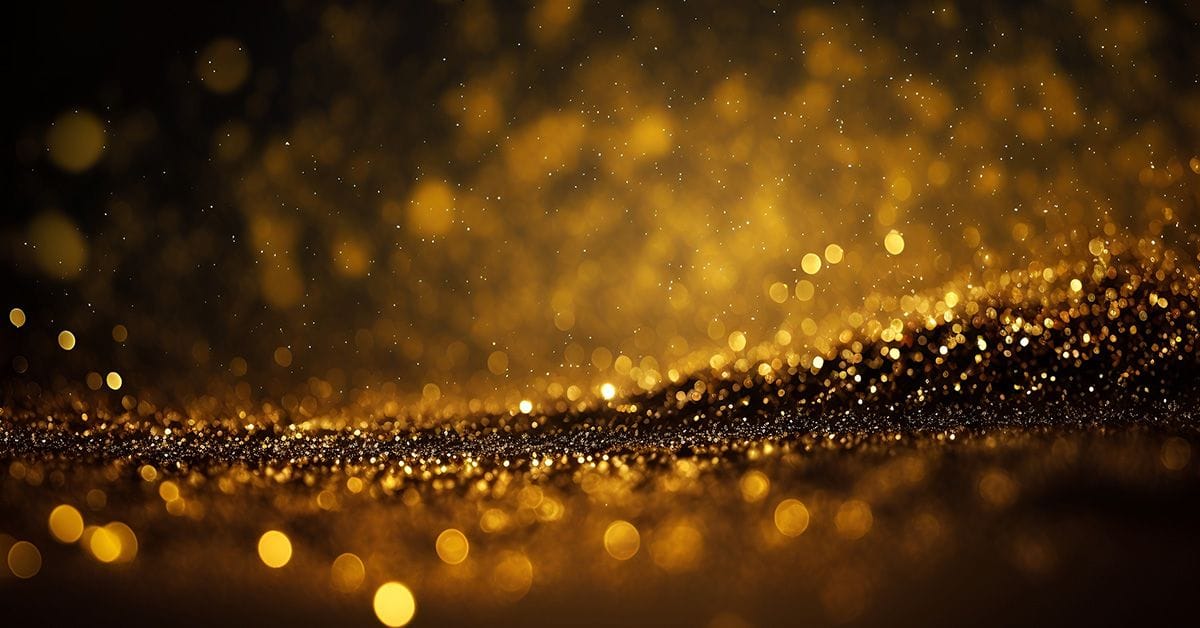 An abstract image of gold glitter particles floating through the air against a blurred dark background, conveying a sense of celebration.