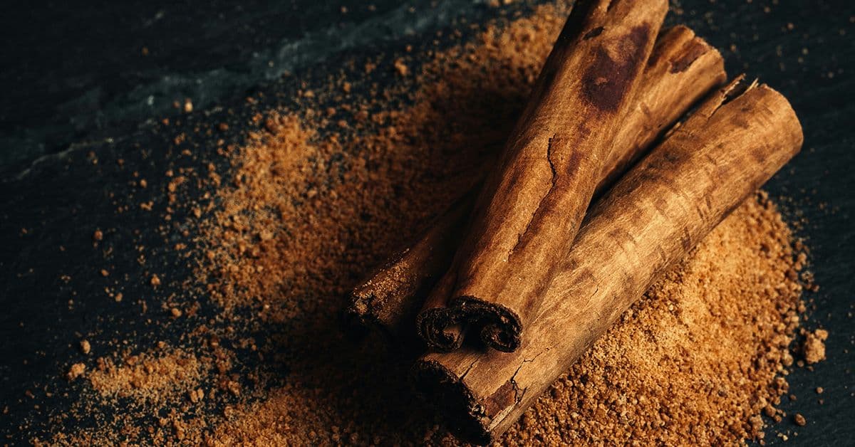 Three cinnamon sticks on top of a mound of powdered cinnamon, set against a dark wooden surface.
