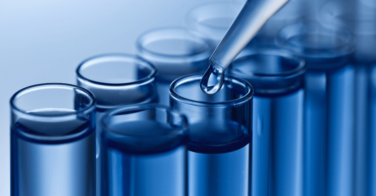 Close‑up of a pipette dispensing a droplet of liquid into a row of blue‑tinted laboratory test tubes.