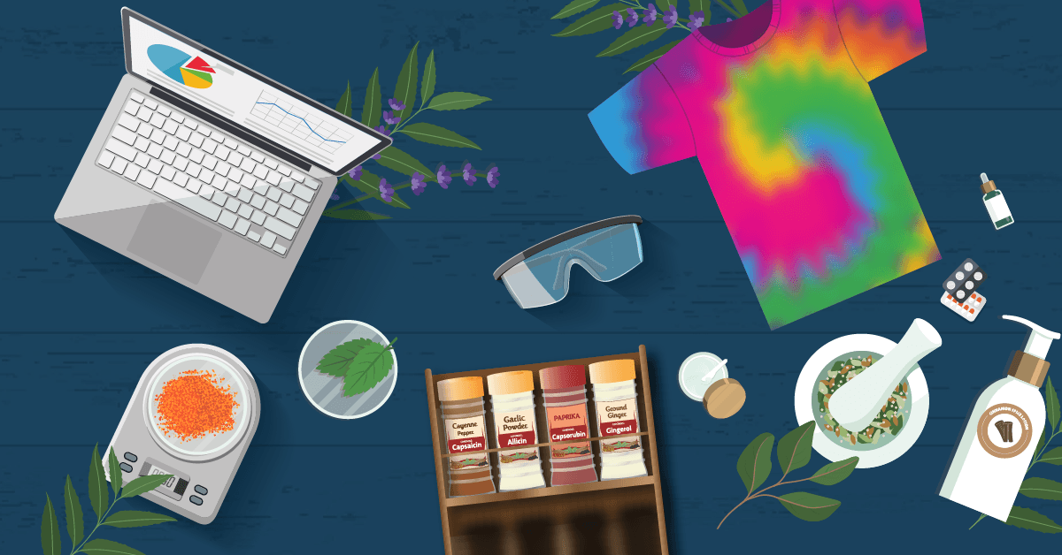 A digital illustration of a top-down view of a workspace with a laptop, tie-dye shirt, spices, herbs, mortar, and various wellness items on a blue wooden table.