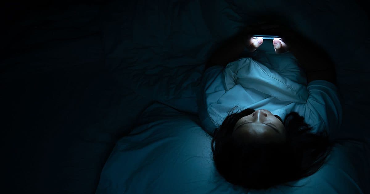 A woman laying in bed with a cell phone in her hand.