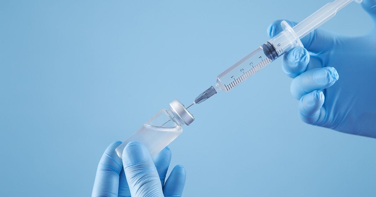 A medical professional with blue gloves holds a syringe and vaccine.