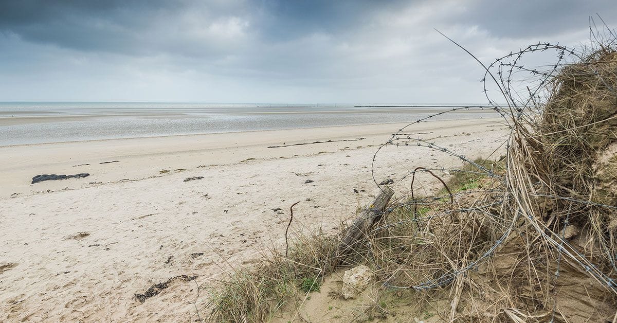 A barbed wire fence on a beach with a cloudy sky.