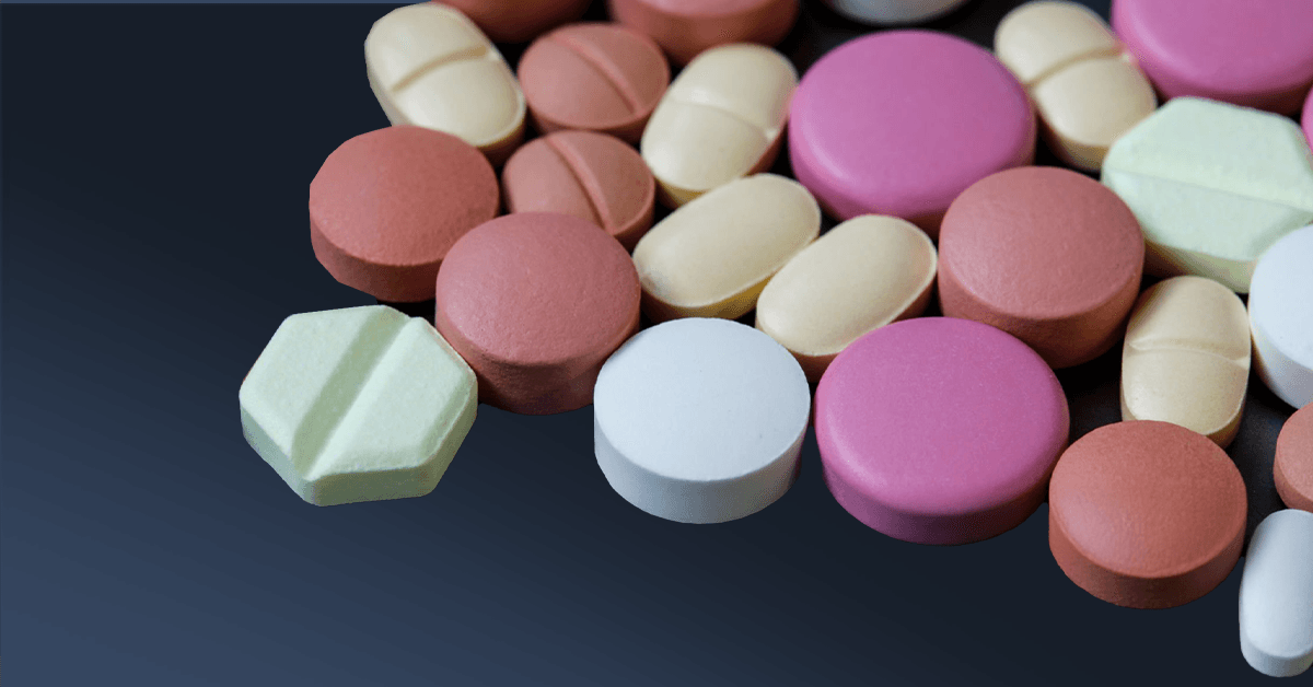 A variety of multicolored medications, including round and oval pills, arranged on a dark background.
