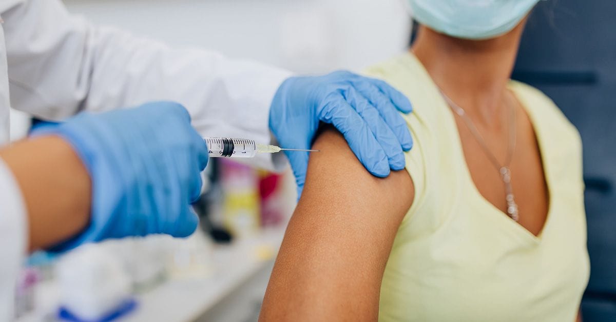 A doctor or nurse giving shot or vaccine to a female patient's shoulder. Vaccination and prevention against flu or virus pandemic.