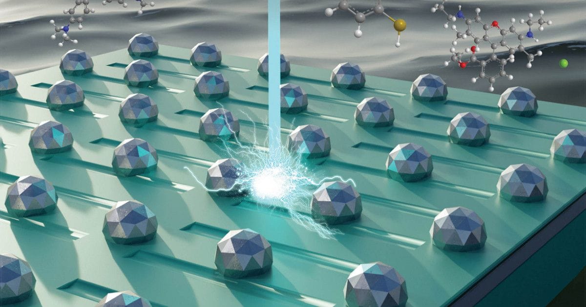 A 3D illustration of geometric silver-toned spheres on a ridged teal surface, with a vertical blue beam meeting one sphere in a bright burst of light, and ball-and-stick molecular models in the dark background.
