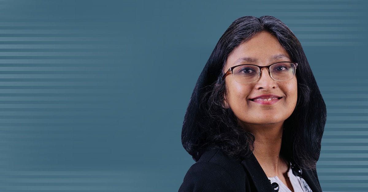 A headshot of Professor Anwesha Sarkar on a dark grayish-teal background