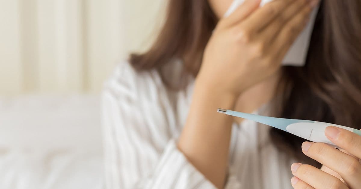a sick woman blowing her nose and reading a thermometer