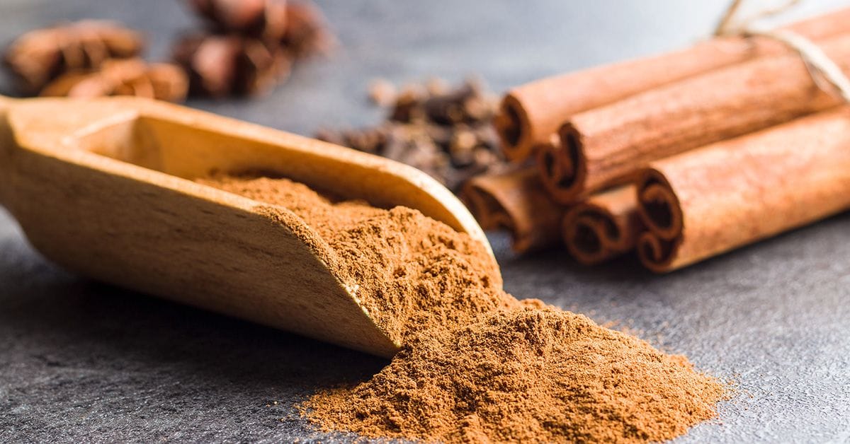 A bundle of cinnamon sticks next to a wooden scoop