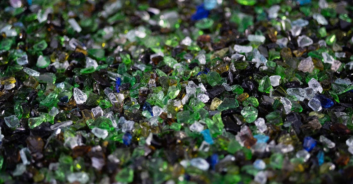 An assortment of multi-colored glass crystals in shades of green, blue, and black, scattered on a dark surface.