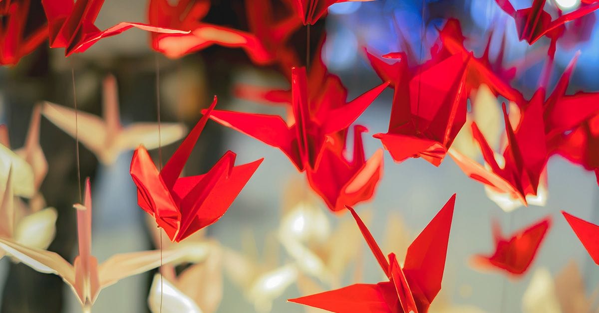 A collection of red and white origami paper cranes suspended in midair.