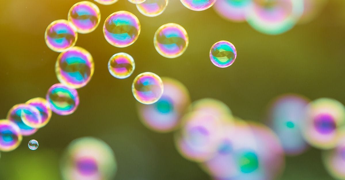 Close-up of iridescent bubbles floating in the air with a softly blurred background, showcasing a spectrum of colors.