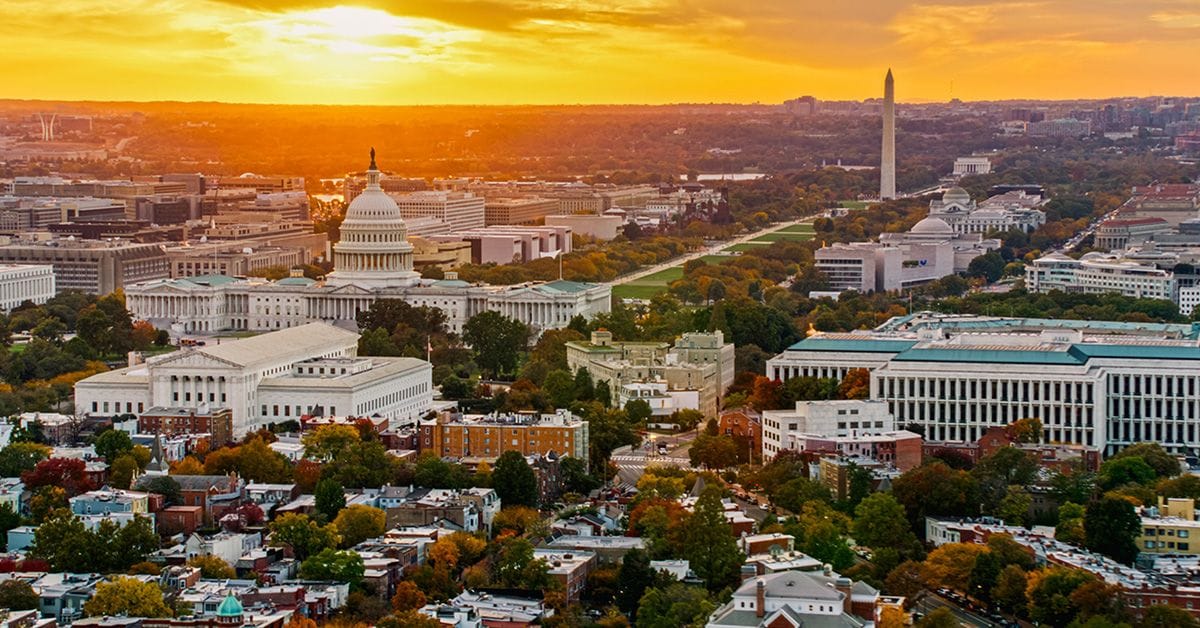 An aerial sunset view of Washington, DC, featuring the US Capitol building and the Washington Monument.