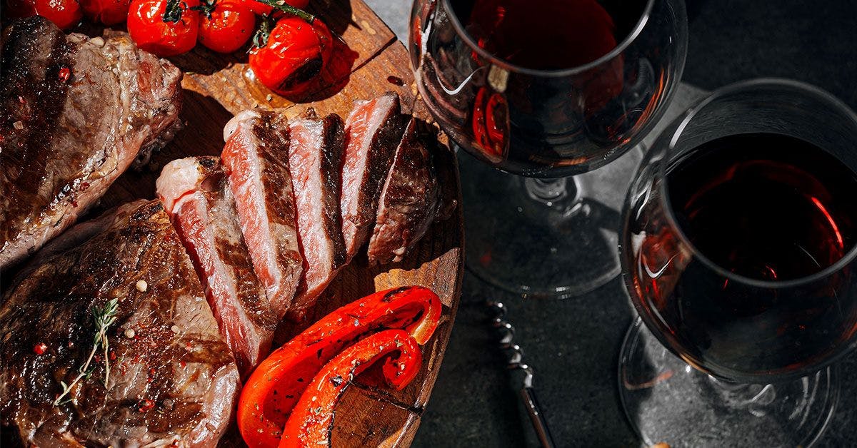 A plate with steak, tomatoes, and red wine.