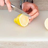 A person cutting a lemon on a cutting board.