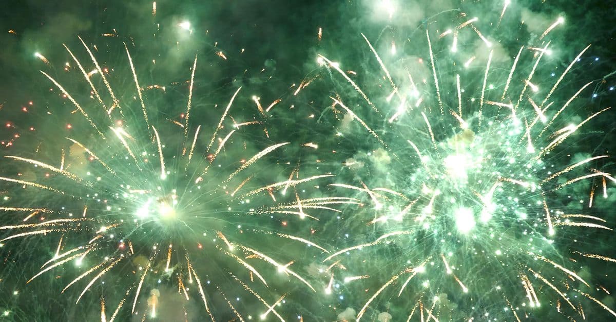 Bright green fireworks explode into the night sky.