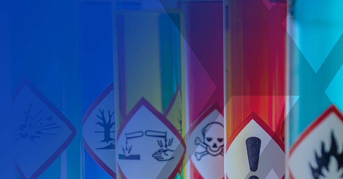 Close-up view of chemical hazard warning labels on glass containers, including symbols for explosive, dangerous to the environment, corrosive, toxic, irritant, and flammable substances.