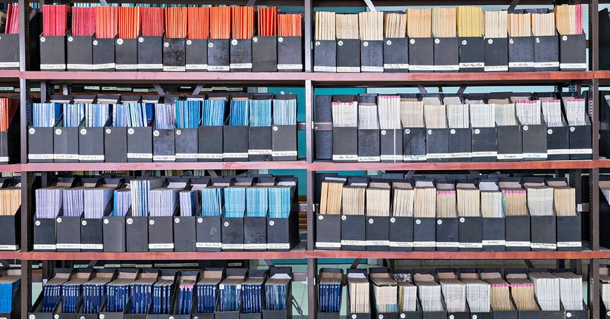 A neatly organized bookshelf displaying various colored binders and boxes filled with labeled documents and folders.