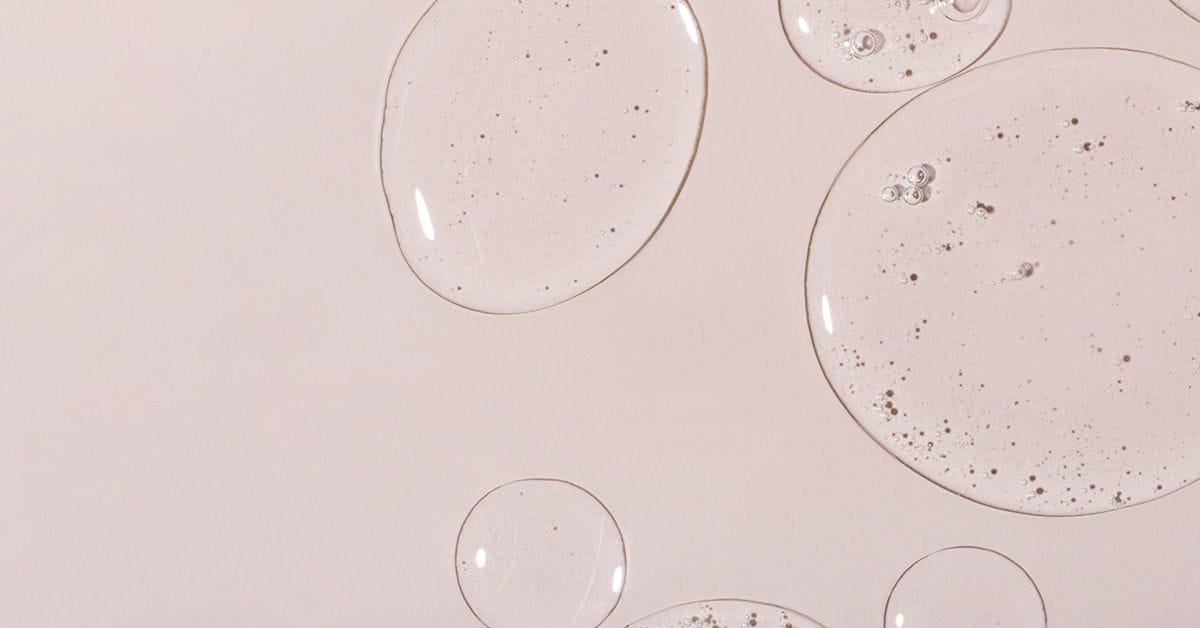 Translucent gel droplets with bubbles on a light pink surface.